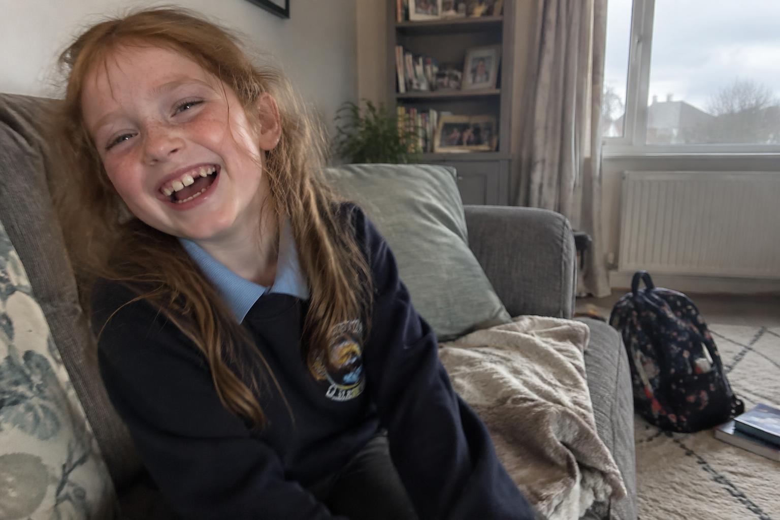 A freckled girl in her school jumper laughing on the sofa