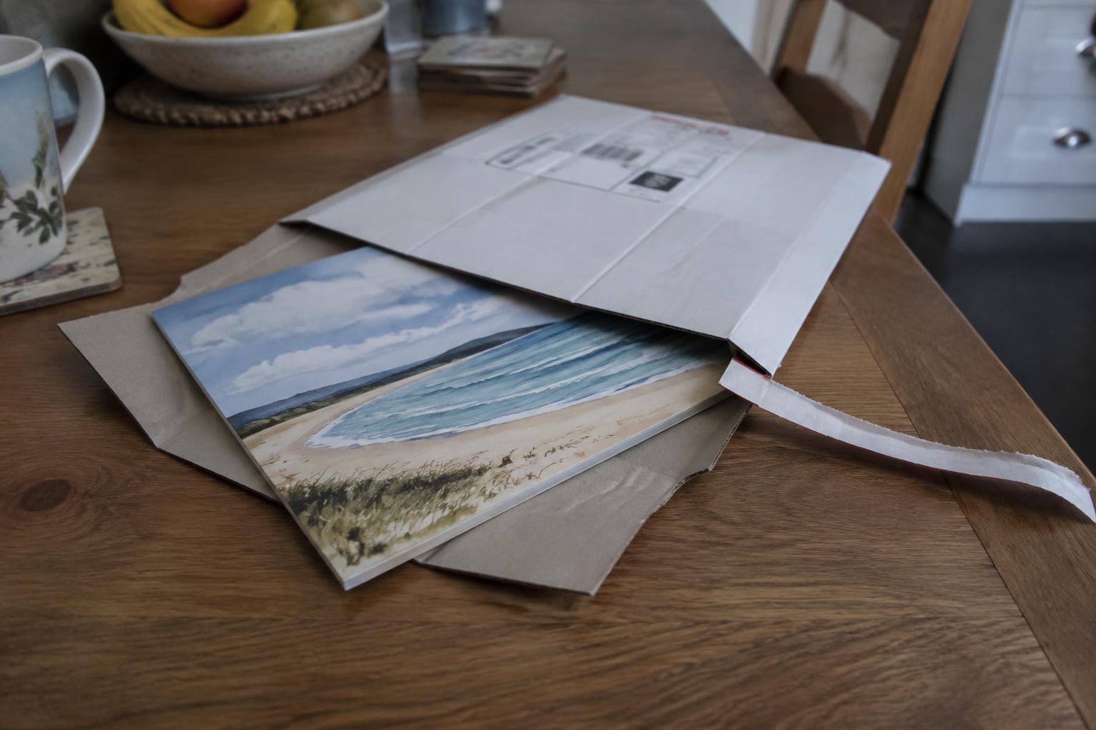 The Story sliding out of its white rigid book mailer on a kitchen table