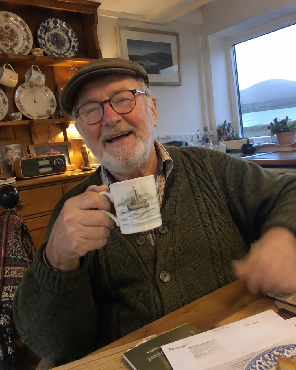 Candid photo of an older man with a white beard, round glasses and tweed cap.